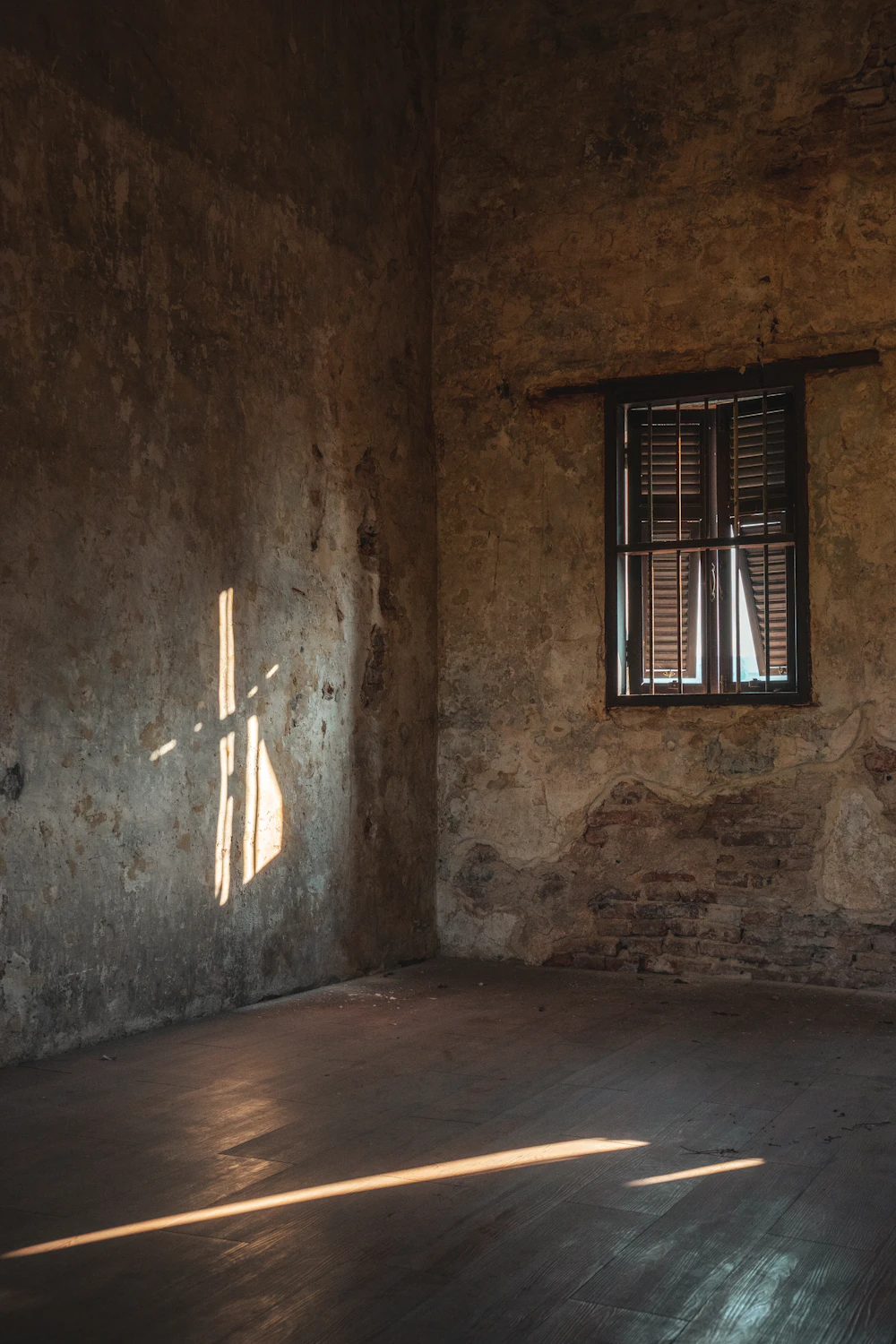 Divisão antiga e vazia, com paredes gastas e uma réstia de luz a entrar pela janela